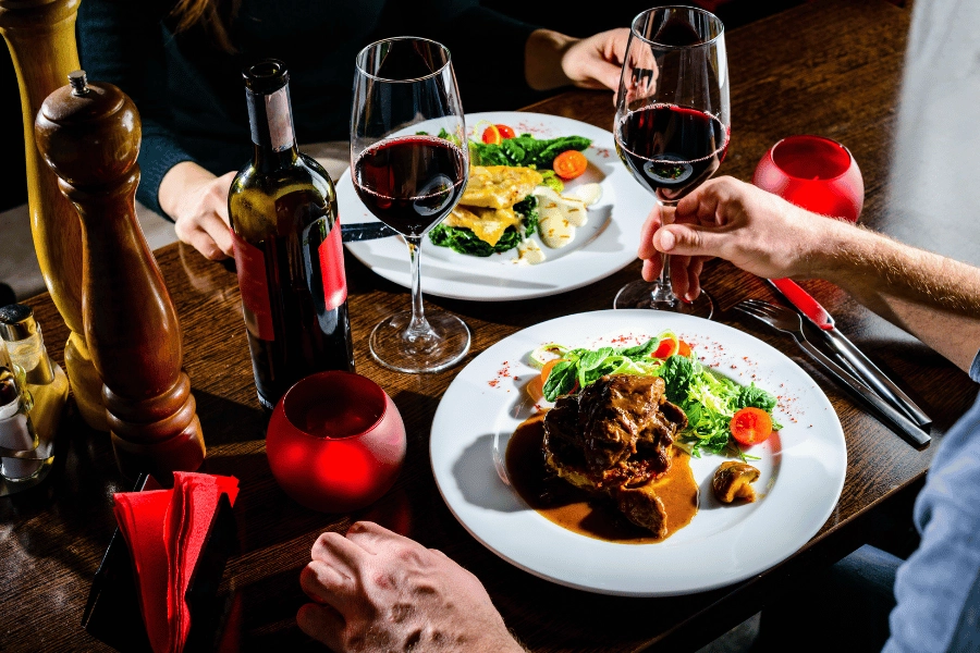 couple enjoying a romantic dinner with delicious food and full glasses of red wine